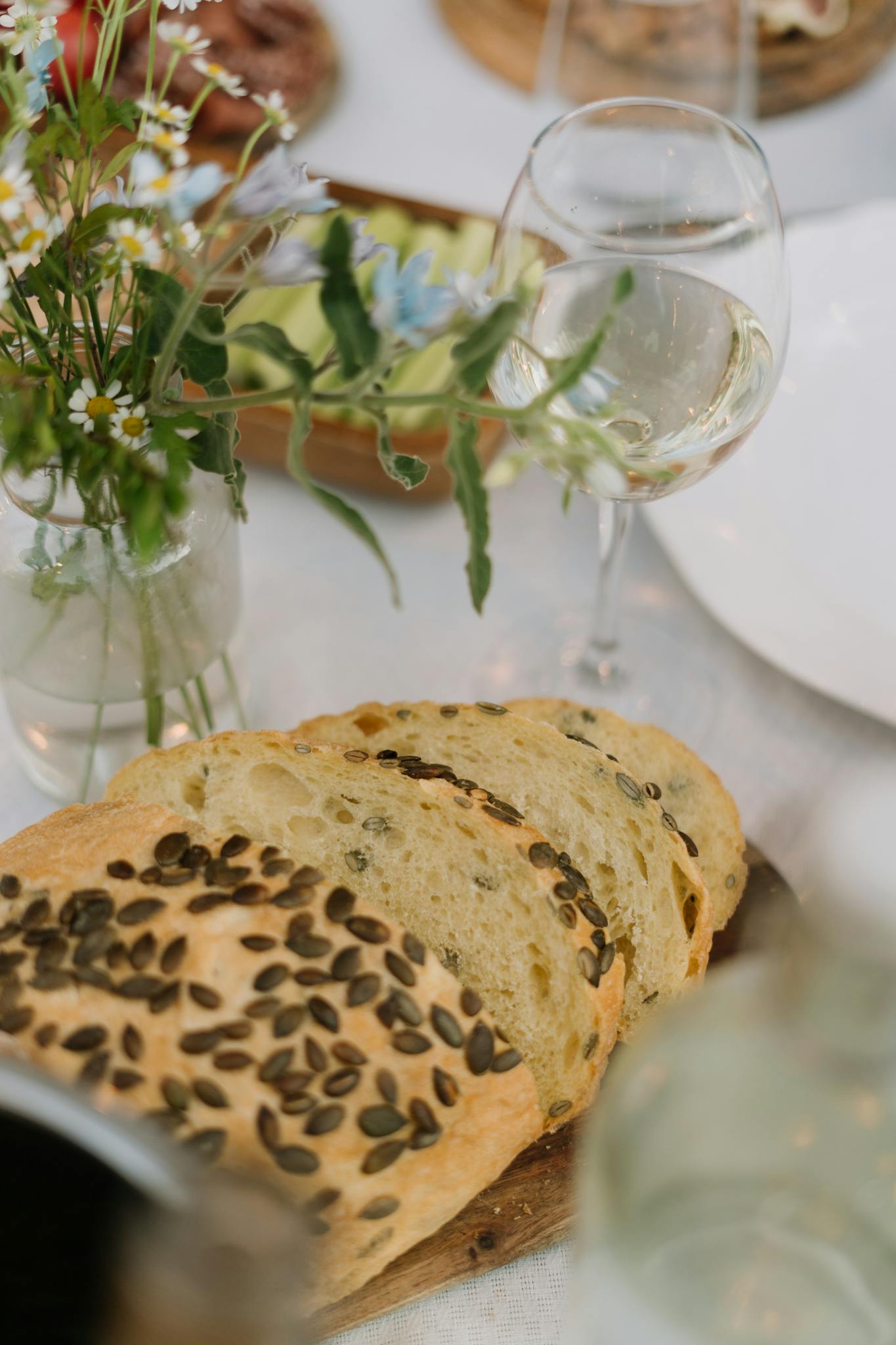 A close-up of sliced bread with seeds paired with a wine glass on an elegantly set table.