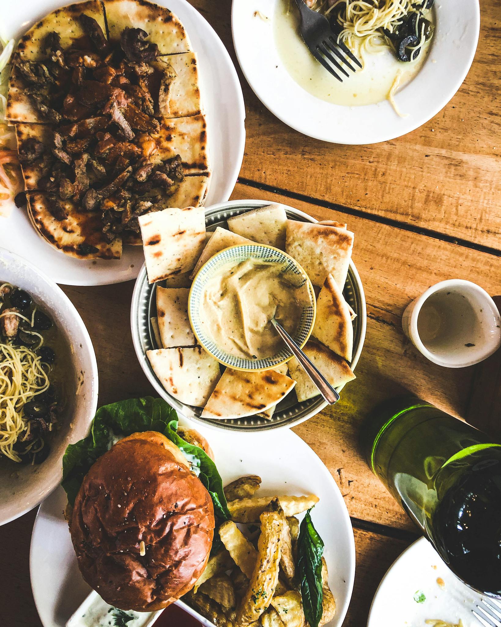A variety of gourmet dishes including flatbread, pasta, and a burger served on a rustic wooden table.